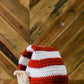 Red and white crocheted elf hat with a beige ear, worn outdoors