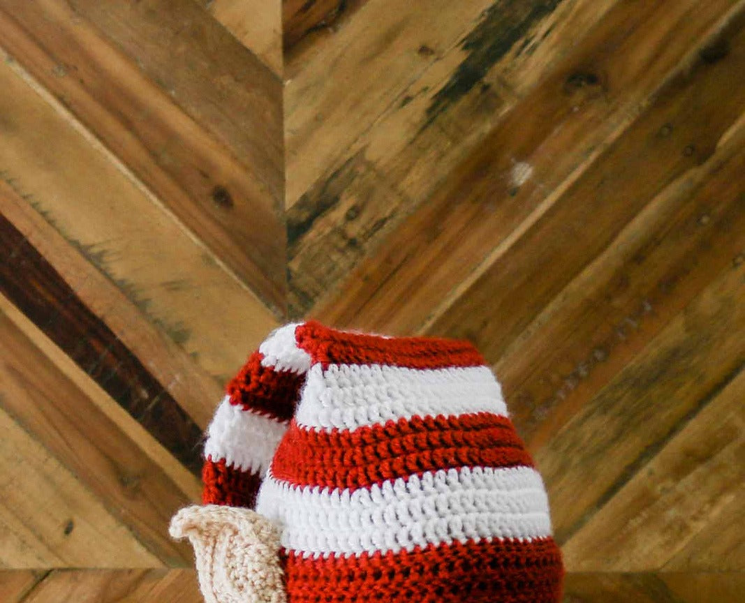 Red and white crocheted elf hat with a beige ear, worn outdoors